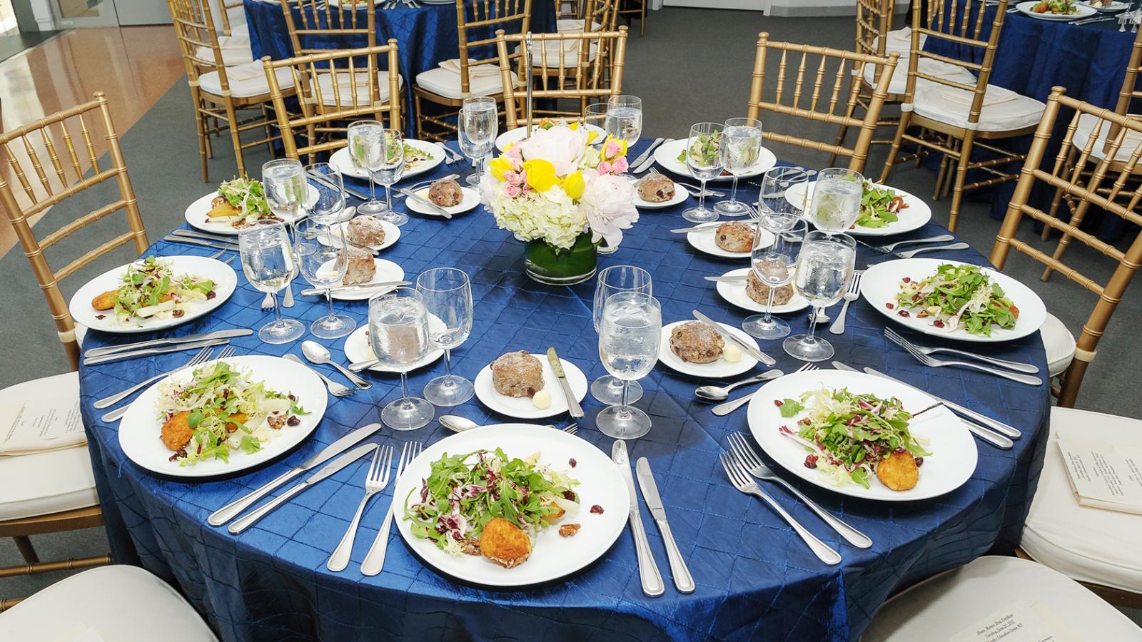 A circular table with blue table-cloth and plated salads