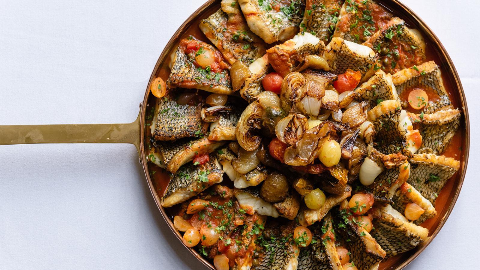 Salmon in a pan with onions, cherry tomatoes, and red sauce.