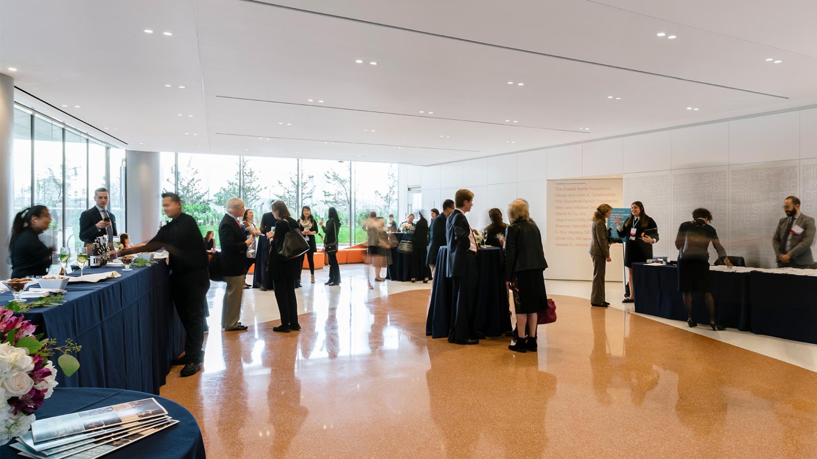People walk around a large event space with wood floors and elegant tables.