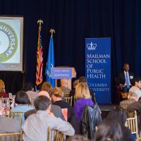 Bard Hall lounge with a panel of speakers, a Powerpoint presentation, and guests seated at tables